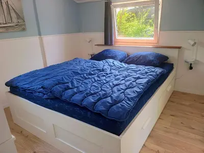 a bed with a blue comforter and a window at Relax Cozy Dirkshorn Stay in Dirkshorn