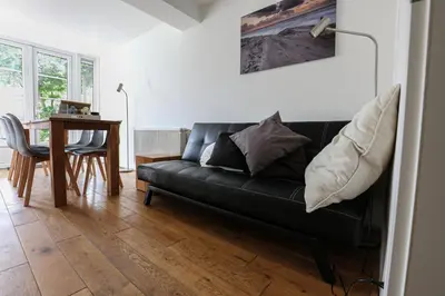 a living room with a black couch and a table at DUINUNDER In de duinen, loopafstand naar 't strand in Noordwijk aan Zee