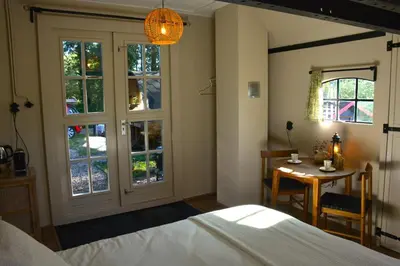 a bedroom with a bed and a table and windows at Bed & Breakfast Puur Natuur Putten, met privé sauna in Putten