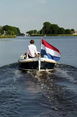 a man in a boat with a flag on the water at Huisje te huur van 15 feb tot 15 mrt voor tweeduizend euro vier weken in Zevenhuizen