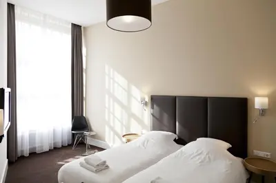 a bedroom with two beds and a large window at College Hotel Alkmaar in Alkmaar