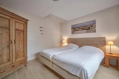 a bedroom with a white bed and a wooden cabinet at Apartments Four Seasons Voorstraat in Egmond aan Zee