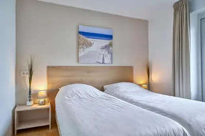 two beds in a hotel room with white sheets at Apartments Four Seasons Voorstraat in Egmond aan Zee