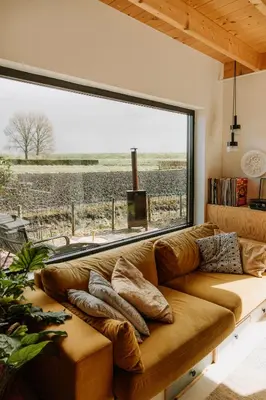 a brown couch in a room with a large window at Sfeervol Vakantiehuis - Badkuip met weids uitzicht - Markermeer - by Familie Buitenhuys holiday houses in Oosterleek