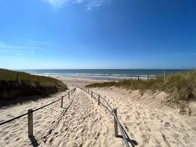 a sandy path to the beach with the ocean in the background at Het Zomerhuis in Zuidbakkum