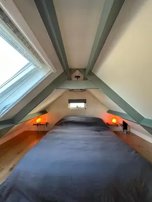a attic bedroom with a large bed with two windows at 't Jisper Huisje in Jisp