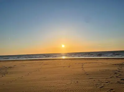 a sunset on the beach with footprints in the sand at Schitterend appartement, 150 m van het strand in Katwijk aan Zee