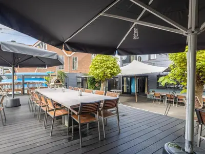 a table with chairs and an umbrella on a deck at De Kaag Watersport Groepsaccommodatie - 80 pers in Kaag