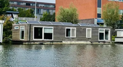 a house with solar panels on the side of a river at Peaceful room on a houseboat in the city centre in Amsterdam