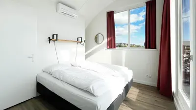 a bedroom with a bed with white sheets and a window at Havenzicht by Droomvilla in Uitgeest