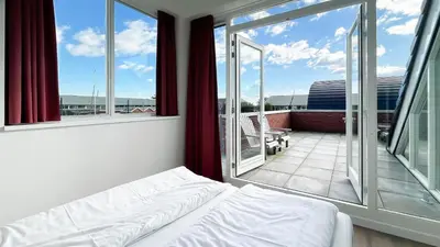 a bedroom with a bed and a balcony with windows at Havenzicht by Droomvilla in Uitgeest