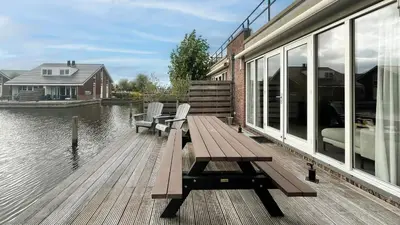 a wooden deck with a bench and chairs on the water at Schelpzicht by Droomvilla in Uitgeest