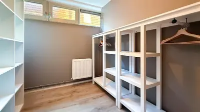 a walk in closet with white shelves and wood floors at Jachtzicht by Droomvilla in Uitgeest