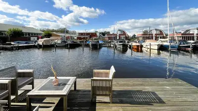 a dock with two chairs and a table and boats at Jachtzicht by Droomvilla in Uitgeest