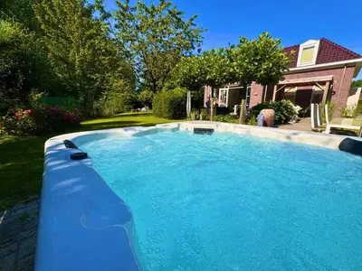 a large blue swimming pool in front of a house at Luxe vakantievilla met jacuzzi in Zeewolde