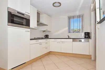 a white kitchen with white cabinets and a window at Vakantiepark Duinrust in Noordwijk