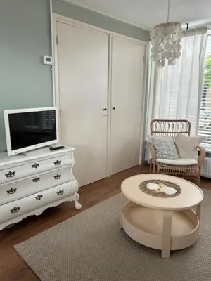 a living room with a dresser with a tv and a table at BeJa bij strand en duin in Egmond aan Zee