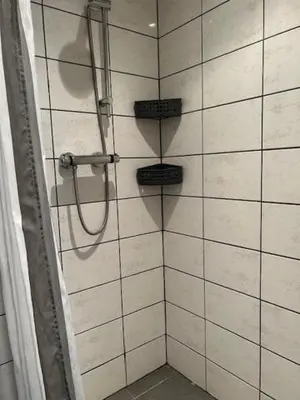 a shower in a bathroom with white tiles at BeJa bij strand en duin in Egmond aan Zee