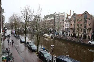 a city street with cars parked next to a river at redlight canalview city centre in Amsterdam