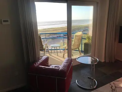 a living room with a chair and a balcony with the ocean at Meerblick Atlantis 17 c in Egmond aan Zee