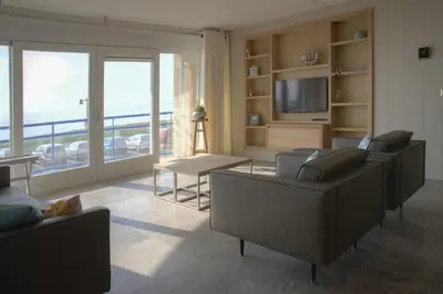 a living room with couches and a television and a balcony at Atlantis 14 in Egmond aan Zee