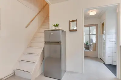 a kitchen with a refrigerator next to a staircase at The White Cottage in Uitgeest