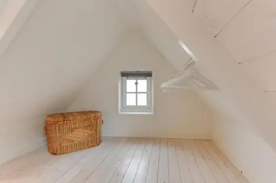 a attic room with a wicker basket and a window at The White Cottage in Uitgeest