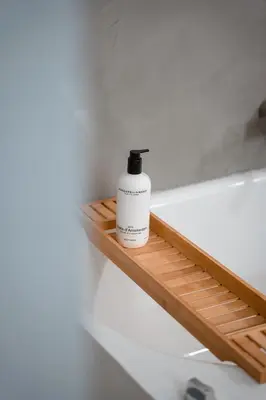 a bottle of soap sitting on a wooden shelf next to a bath tub at Court Hotel Utrecht City Centre in Utrecht