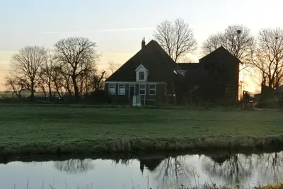 an old house on a field next to a lake at Appartement Voorhuis en chalet Klein Waterland in Amsterdam