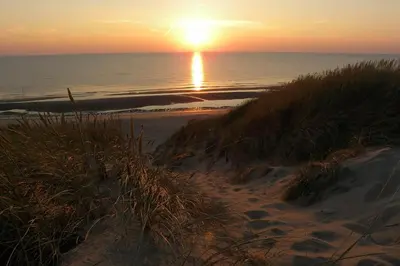 a sunset on a beach with the ocean and the sand at Gestrand in Egmond aan Zee