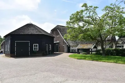a black barn with a tree and a driveway at Chalet 4, Recreatie aan de Vecht in Weesp