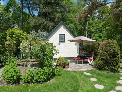 a small white house with an umbrella and a patio at Kleine Nachtegaal in Schoorl