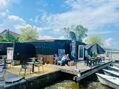 a couple sitting on a dock next to a boat at Houseboat Oslo perfect voor bezoek Amsterdam in Monnickendam