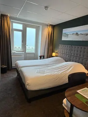 a bedroom with a large bed and a table at Hotel Zee en Duin in Katwijk