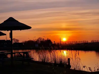 a sunset with a table and an umbrella next to a pond at Safari Lodges Premium in Nieuwe Wetering