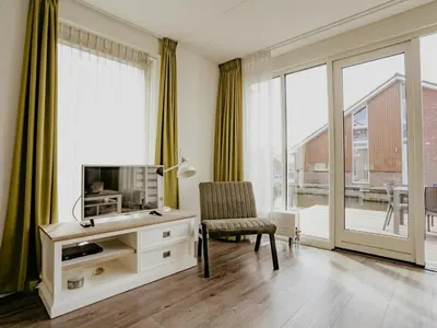 a living room with a tv and a chair at Spacious Lakeside Retreat in Uitgeest