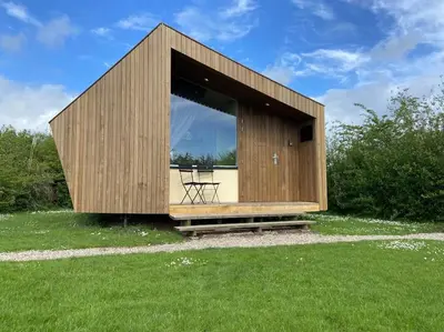 a small wooden building with a chair in a field at Design huisje vrij in het groen in IJsselstein