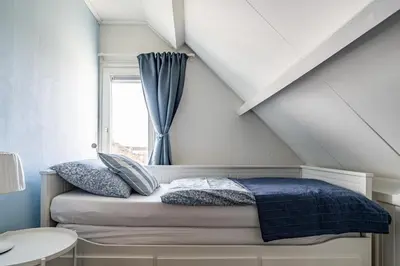 a bedroom with a bed with blue sheets and a window at Huisje Bloemenzee in Noordwijkerhout
