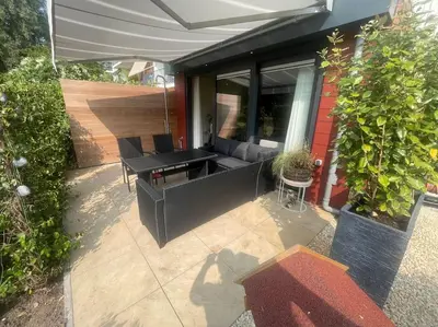 a patio with a couch and a table and an umbrella at Luxe appartement bij Zuidas met tuin en buitendouche in Amsterdam