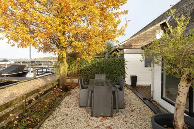 a table and chairs under a tree next to a house at Woonboot De Rietpieper in Loosdrecht