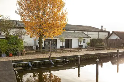 a house with a tree next to a river at Woonboot De Rietpieper in Loosdrecht