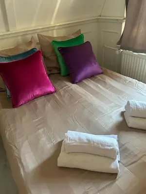 a white bed with purple and green pillows on it at Cosy by Mandy in Amsterdam