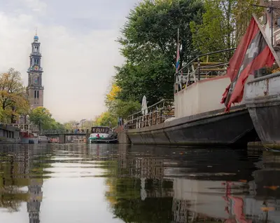two boats are docked on a river with a clock tower at Skinny Bridge Boutique Stay in Amsterdam