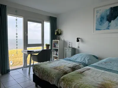 a bedroom with a bed and a desk and a window at Appartement Atlantis met Zeezicht in Egmond aan Zee
