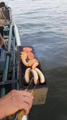 a person cooking hot dogs on a grill on a boat at Tjalkjacht Pelikaan Hoorn in Hoorn