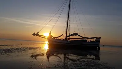 a boat sitting on the beach at sunset at Tjalkjacht Pelikaan Hoorn in Hoorn