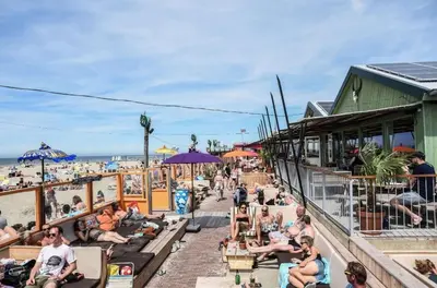 a group of people sitting on a boardwalk near the beach at Smile Home Wijk aan Zee 1 in Wijk aan Zee