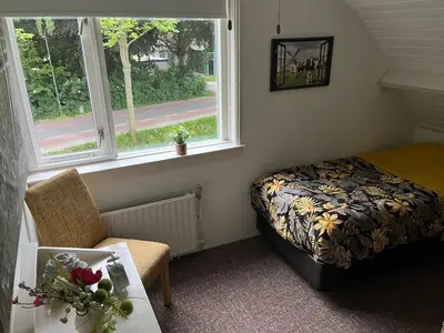 a bedroom with a bed and a chair and a window at B&B Dol - Fijn in Benningbroek