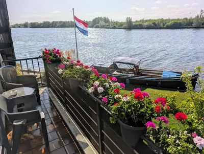 a balcony with flowers and a boat on the water at 1-2 pp ROOM AMS Airport great view lake in Roelofarendsveen