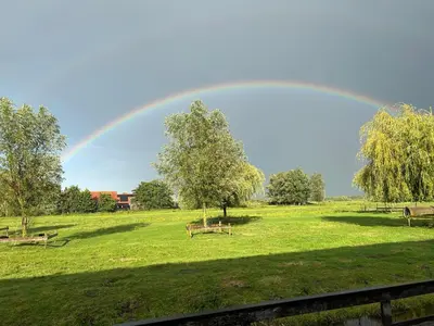 a rainbow in the sky over a field with benches at Zaanse Rietveld Logies in Alphen aan den Rijn